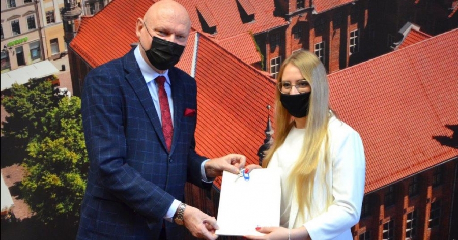 Klucze wraz z umowami najmu wręczył laureatom programu prezydent Michał Zaleski podczas spotkania, które 21 grudnia odbyło się w Urzędzie Miasta fot.Natalia Przytarska | Urząd Miasta Torunia prezydent miasta wręczający klucze absolwentce, w tle zdjęcie toruńskiego ratusza