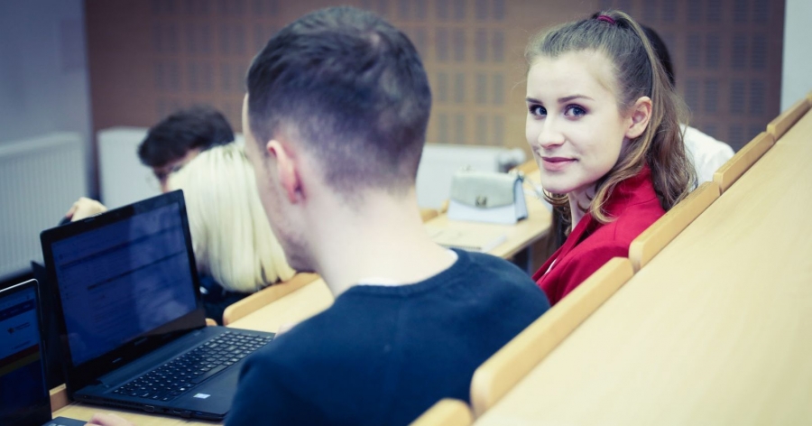 fot.fot. Andrzej Romański Sala wykładowa, studentka patrzy w obiektyw aparatu, w tle inni studenci uczestniczą w zajęciach