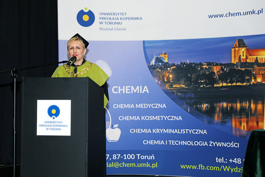 Dyplomatorium WCh UMK na zdjęciu dziekan Wydziału Chemii podczas przemówienia, w tle baner wydziału