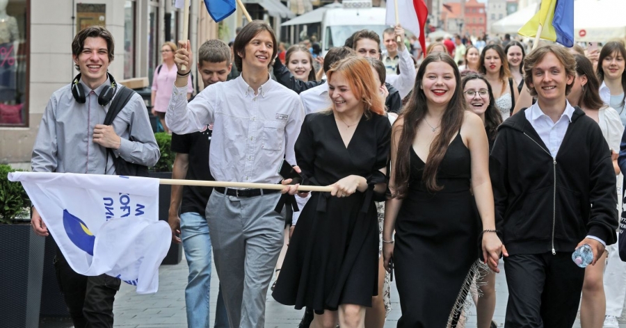 Spotkania studentów i studentek z "Zerówki" zaowocowały stworzeniem aktywnego zespołu integrującego się z międzynarodową społecznością akademicką fot.Andrzej Romański Grupa osób na wspólnym marszu przez ulice starówki. W pierwszy rzędzie idzie trzech mężczyzn i dwie kobiety. Osoba na środku trzyma flagę z logo UMK, w tle widać osoby niosące flagi innych krajów