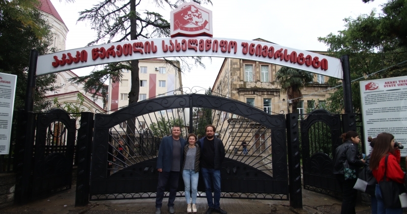 Three people against the background of the entrance gate and university buildings