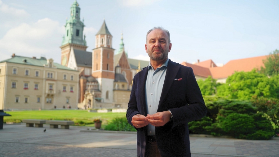 Profesor Jarosław Dumanowski na planie serialu fot.nadesłane Mężczyzna w średnim wieku stojący na tle skweru z zielenią i zabytkowych budowli kościelnych.