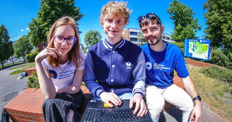 Class evaluation questionnaires will remain open until September 30, 2024 photo:Photo: Andrzej Romański A female student and two male students are sitting next to each other, outside. The student sitting in the middle holds a laptop on his lap. The students are wearing clothes with the UMK logo