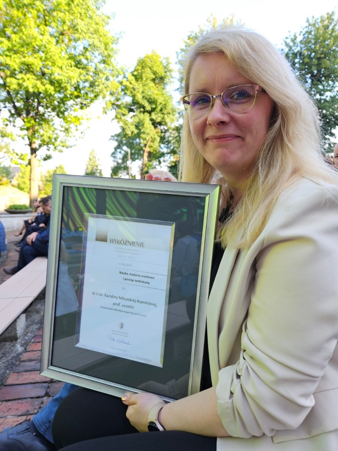 dr hab. Karolina Mikulska-Rumińska, prof. UMK fot.prof. dr hab. Ireneusz Grabowski Uśmiechnięta dr hab. Karolina Mikulska-Rumińska trzymająca oprawione wyróżnienie.