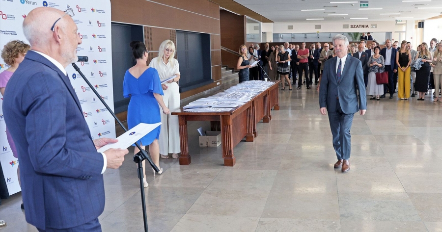 Uroczystość wręczenia nagród pracownikom naukowym odbyła się 1 lipca w foyer Auli UMK fot.fot. Andrzej Romański Po lewej stronie stoi JM Rektor z teczką, a w jego stronę idzie mężczyzna w garniturze. W tle widać grupę stojących osób