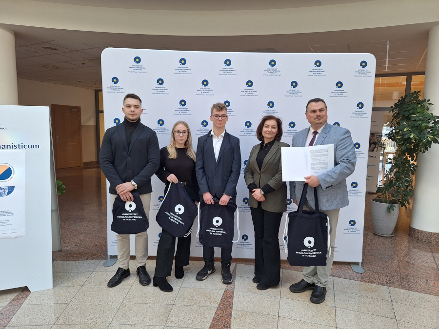 Podpisanie porozumienia o współpracy z III Liceum Ogólnokształcącym w Grudziądzu fot.Izabela Kujawska troje uczniów, Pani Prodziekan dr hab. Inga Głuszek prof. UMK i Dyrektor IIILO w Grudziądzu pozują z podpisanyym porozumieniem o spółpracy na tle ścianki z logo WNH
