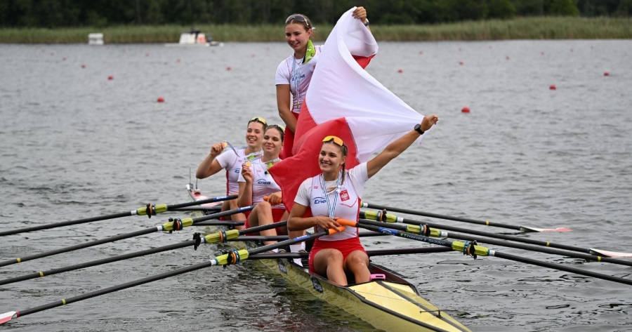 Osada reprezentantek Polski przekroczyła metę jako pierwsza, wyprzedzając reprezentację Czech i Wielkiej Brytanii fot.Julia Kowacic/PZTW Zawodniczki siedzą w łodzi po zwycięskim biegu, na szyjach mają medale, trzymają także polską flagę, jedna zawodniczka stoi