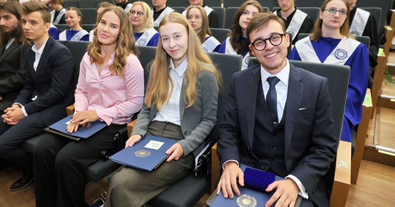 Dwie studentki i jeden student - uśmiechnięci i eleganccy siedzą w pierwszym rzędzie auli UMK