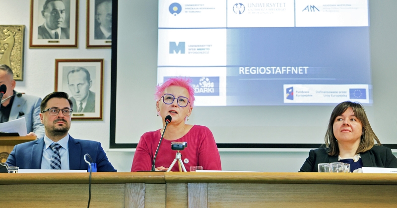 Za stołem przy mikrofonach siedzą trzy osoby. Dwie kobiety i jeden mężczyzna. Trwa konferencja prasowa.