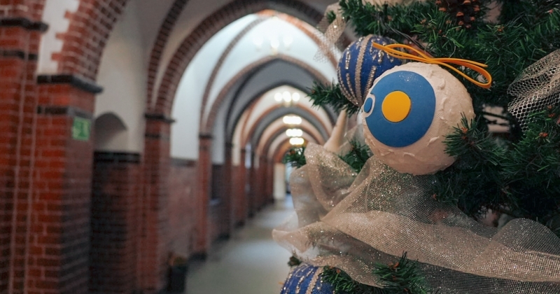 Choinka w na korytarzu Collegium Maius ubrana w bombki z logo UMK.