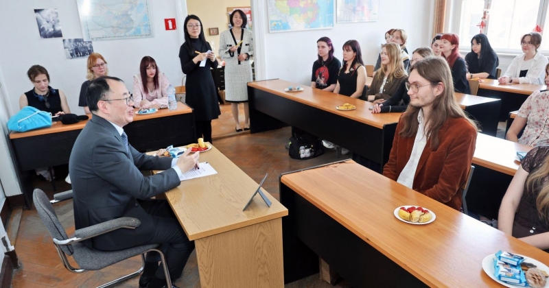 Sala wykładowa, ambasador siedzi przy biurku wykładowcy, studenci i studentki w ławkach. Widać uśmiechy i życzliwą atmosferę spotkania