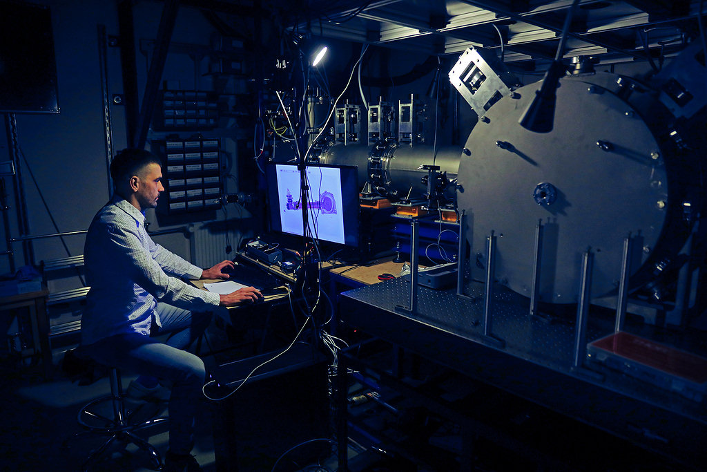 A scientist sitting at the console of a large research apparatus [photo: Andrzej Romański]