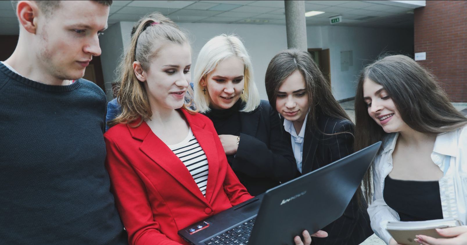 Grupa student&oacute;w wpatrujących się w ekran laptopa.