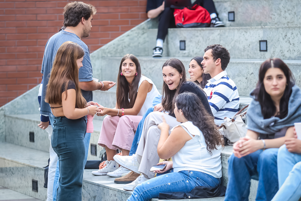 Zdjęcie przedstawia roześmianych studentów siedzących i rozmawiających na schodach przed rektoratem UMK.