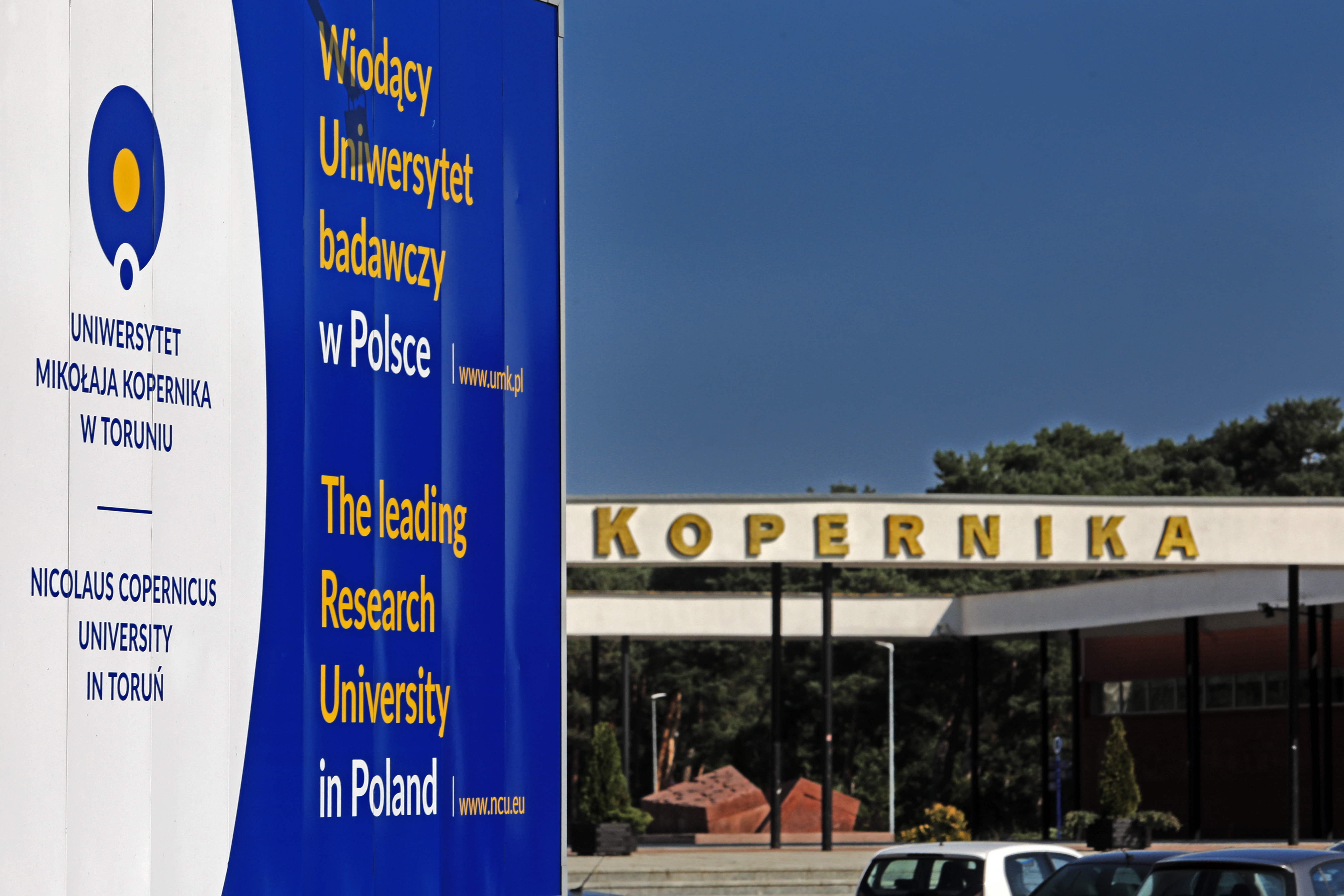 Zdjęcie tablicy z napisem Wiodący Uniwersytet Badawczy, w tle budynki UMK