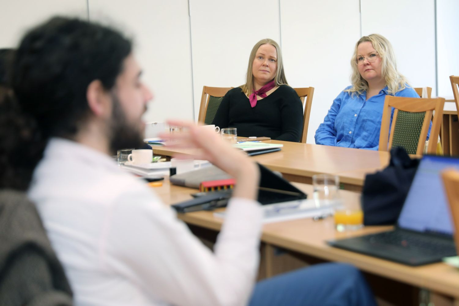 One person is speaking; the two sitting on the other side of the table are listening intently