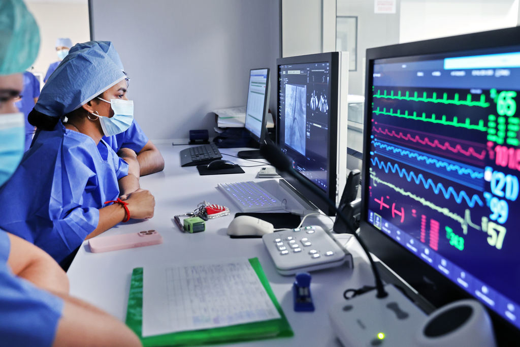 peope in medical uniforms sit in front of computers with scientific data on the screens