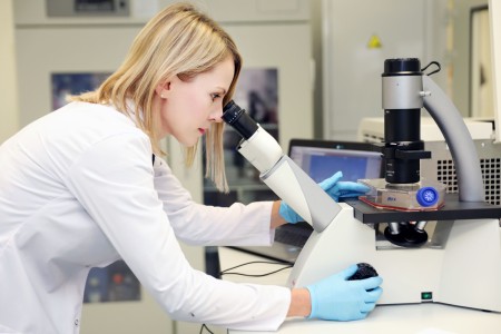 Autorka artykułu w sali laboratoryjnej. Spogląda przez obiektyw specjalistycznego sprzętu. W tle komputer i inne urządzenia.. Kliknij, aby powiększyć zdjęcie.