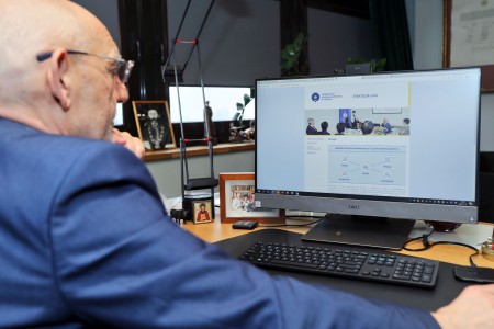 JM Rektor siedzący w gabinecie przy biurku z komputerem stacjonarnym. Na ekranie wyświetlony dokument Strategii UMK. Widoczny fragment prawego profilu postaci.  . Kliknij, aby powiększyć zdjęcie.