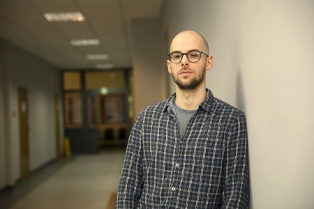 Dr inż. Jakub Rydzewski stojący na korytarzu Instytutu Fizyki. Kliknij, aby powiększyć zdjęcie.