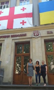 Na zdjęciu znajdują się trzy osoby, w środku Rusudan Janjibukhashvili szefowa zespołu języka angielskiego A2, po jej prawej stronie Katarzyna Gałka, wykładowca języka angielskiego UMK,  po lewej Joanna Wińska, wykładowca UMK. W tle znajduje się wejście do budynku Ilia State University w Tbilisi. Kliknij, aby powiększyć zdjęcie.