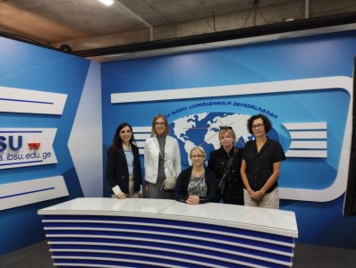 A group of lecturers with a representative of IBSU University stands behind the presenter's counter and poses for a photo.. Click to zoom the picture.