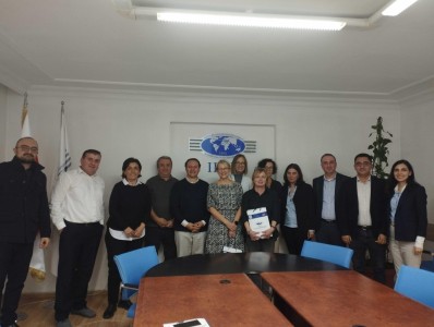 In the photo, a group of employees of the Faculty of IBSU Business and Management pose for a photo against the background of a roll-up with the university logo in the faculty council room. In the foreground, connected tables.. Click to zoom the picture.