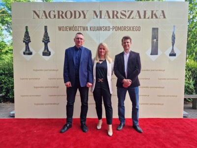 Prof. dr hab. Ireneusz Grabowski, dr hab. Karolina Mikulska-Rumińska, prof. UMK, dr Daniel Rumiński stoja na tle ścianki z napisem Nagrody Marszałka województwa kujawsko-pomorskiego.. Kliknij, aby powiększyć zdjęcie.