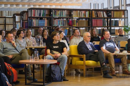 Zdjęcia sali biblioteki wydziału, na których widzimy siedzących słuchaczy i prelegentkę i jej prezentację . Kliknij, aby powiększyć zdjęcie.