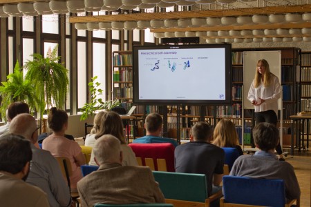 Seminarium w bibliotece Wydziału Chemii. Prelegentka na tle ekranu multimedialnego referuje. Pracownicy i studenci Wydziału siedzą na przeciwko niej i słuchają interesującego wykładu.. Kliknij, aby powiększyć zdjęcie.