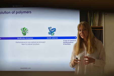 Seminarium w bibliotece Wydziału Chemii. Prelegentka na tle ekranu multimedialnego referuje. Pracownicy i studenci Wydziału siedzą na przeciwko niej i słuchają interesującego wykładu.. Kliknij, aby powiększyć zdjęcie.