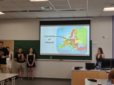 Na pierwszym planie grupa uśmiechniętych studentów oraz nauczycieli stojących w szeregu na tle wejścia do budynku Uniwersytetu Cypryjskiego.. Kliknij, aby powiększyć zdjęcie.