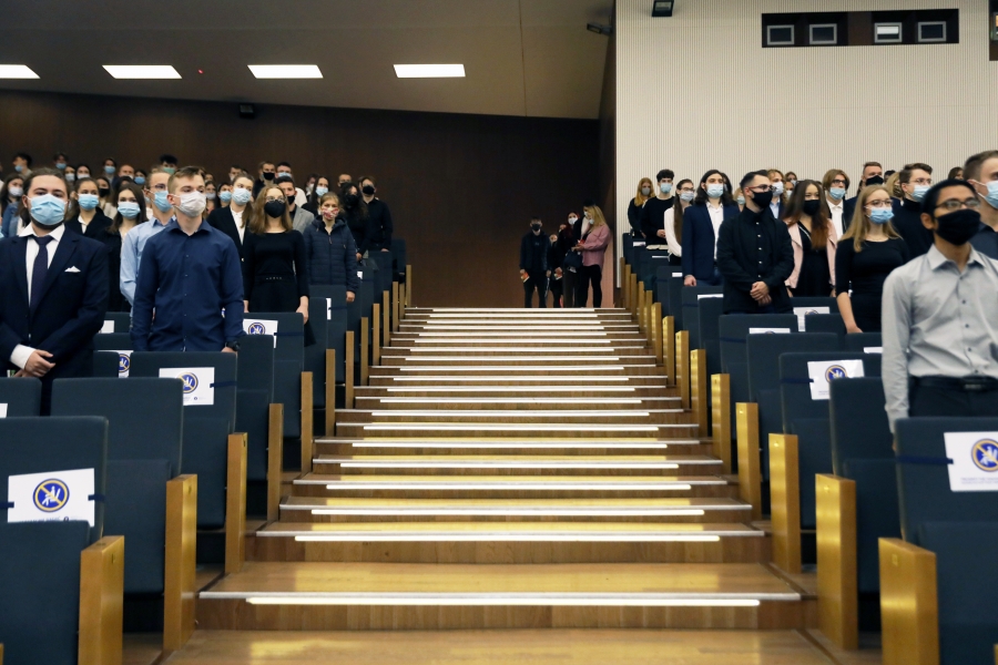 Stojący ludzie w Auli UMK, po środku schody, wszyscy w maseczkach (w trakcie hymnu)