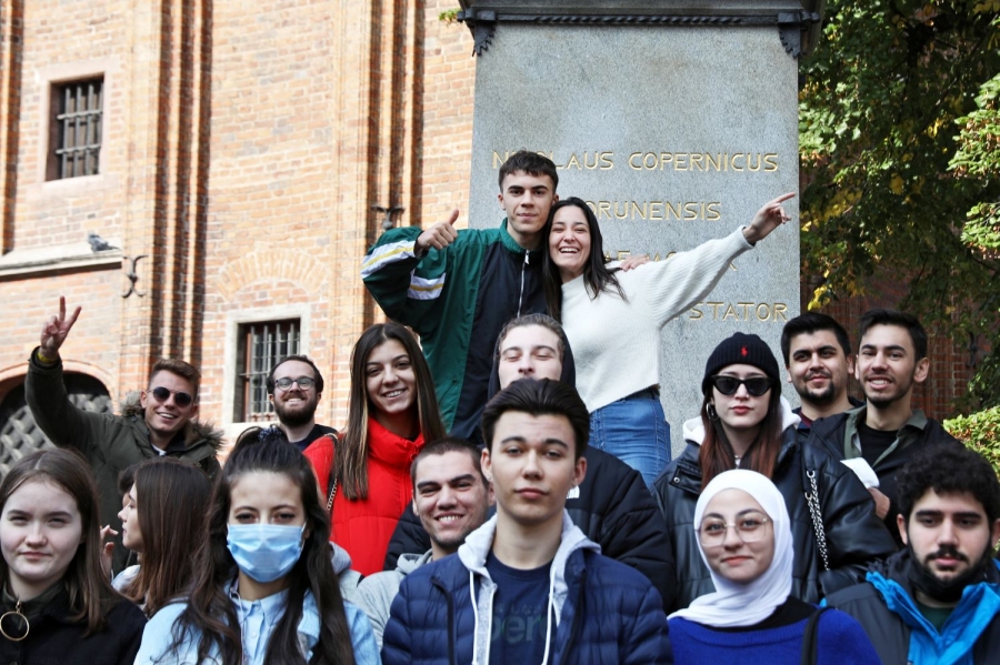 Grupa młodych osób z różnych państw stojąca na tle pomnika Mikołaja Kopernika w Toruniu
