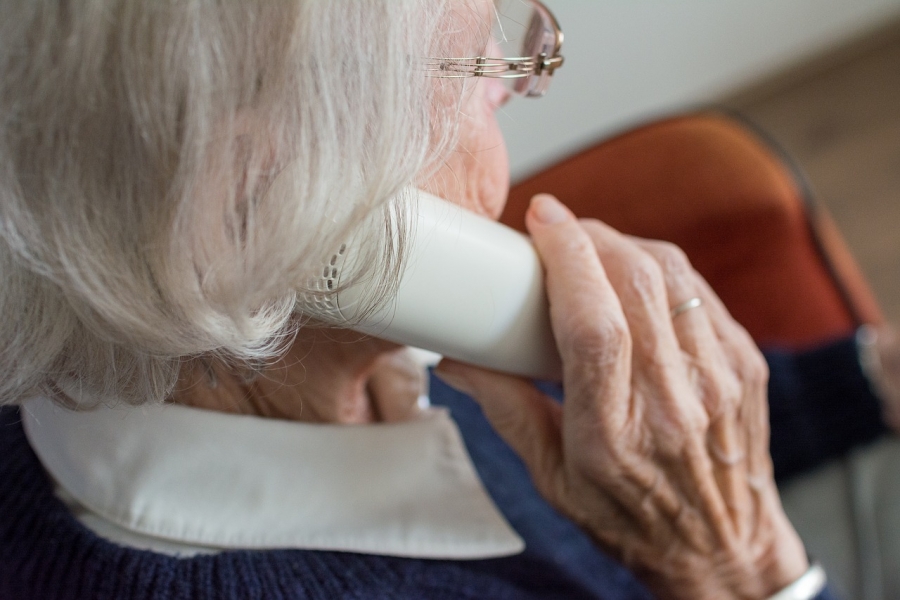Starsza kobieta trzymająca przy uchu słuchawkę telefonu. Widok fragmentu głowy i prawej dłoni.