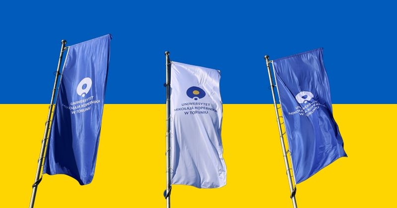 in the photo there are three flags with the logo of the university, in the background the flag of Ukraine