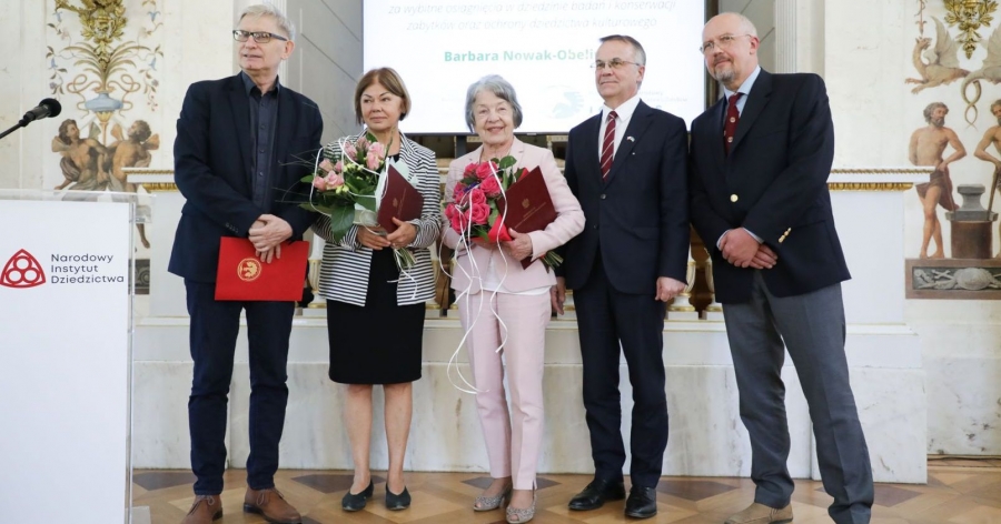 Pięcioro ludzi pozuje do zdjęcia podczas uroczystości wręczenia Nagród im. prof. Jana Zachwatowicza. Po lewej stronie stoi pulpit z napisem Narodowy Instytut Dziedzictwa