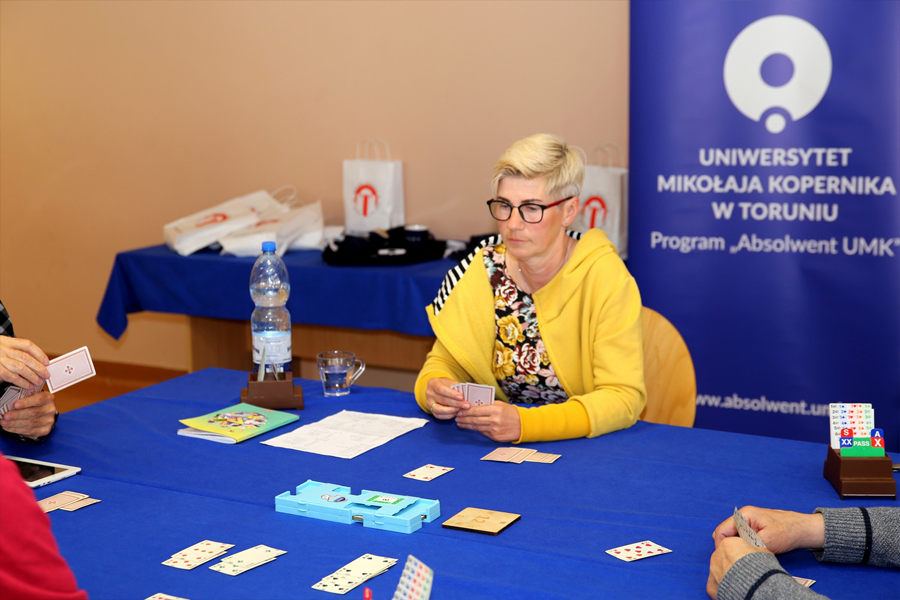 na zdjęciu uczestniczka turnieju brydżowego z kartami przy stole