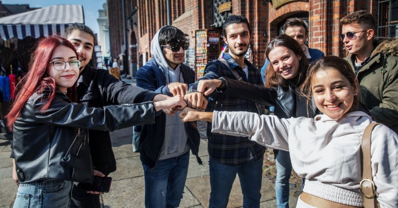 A group of international students give themselves a fist-pumps. They are standing near Toruń town hall.