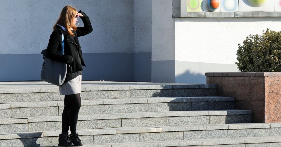 Dziewczyna stoi przed Aulą UMK, przykłada rękę do czoła, żeby osłonić oczy przed słońcem