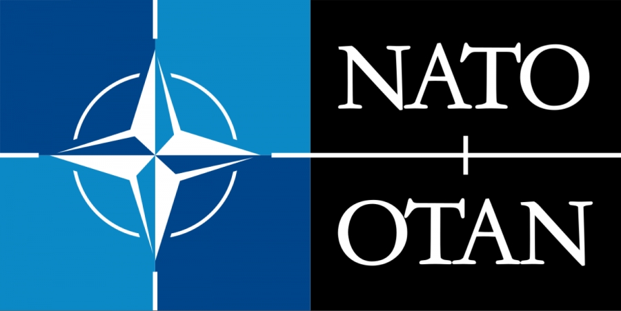 Logo NATO: poziomy prostokąt złożony z dwóch kwadratów. Pierwszy kwadrat złożony z 4 o dwóch odcieniach niebieskiego ułożonych naprzemiennie. W środku znajduje się czteroramienna gwiazda NATO. Drugi kwadrat ma czarne tło i jest w posiomie przedzielony białą linią. Powyżej tej linii widnieje biały napis NATO, poniżej linii biały napis OTAN. Każdy z tych napisaów składa się z duzych liter. 
