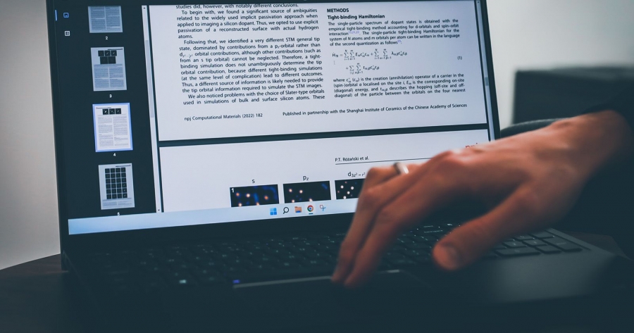 Laptop z wyświetlonym artykułem naukowym na ekranie. Widać również dłoń na klawiaturze.