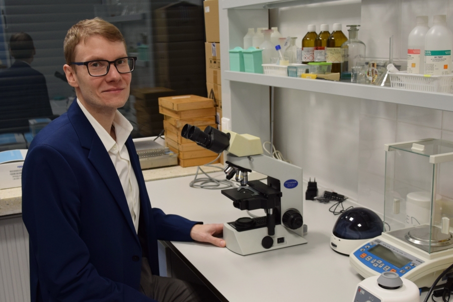 dr Krzysztof, lekko uśmiechnięty, obok swojego ulubionego mikroskopu 