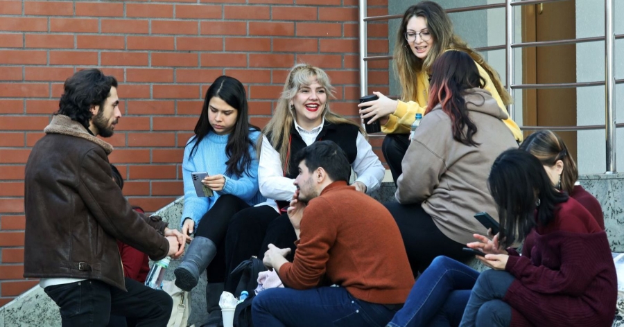 Grupa studentów i studentek siedzi na schodach i rozmawia ze sobą. Na zdjęciu jest osiem osób.