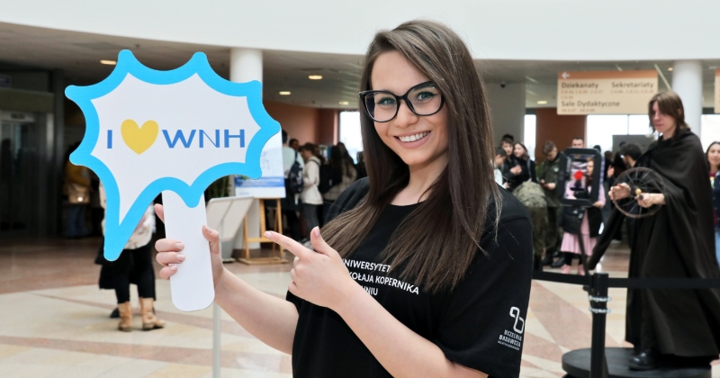 Młoda kobieta wskazuje na trzymany napis "I love WNH"