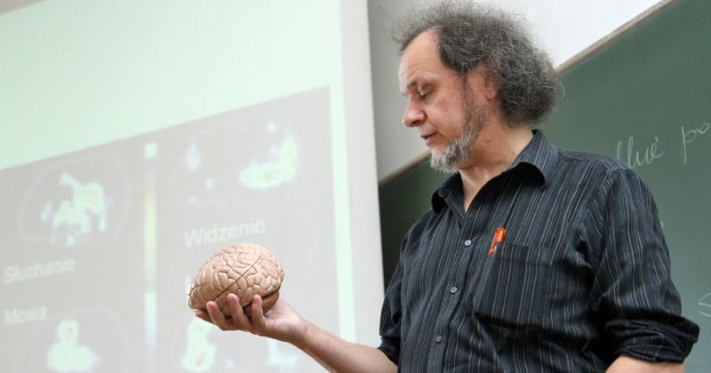 Prof. dr hab. Włodzisław Duch trzyma w lewej ręce sztuczny mózg i patrzy na niego. 