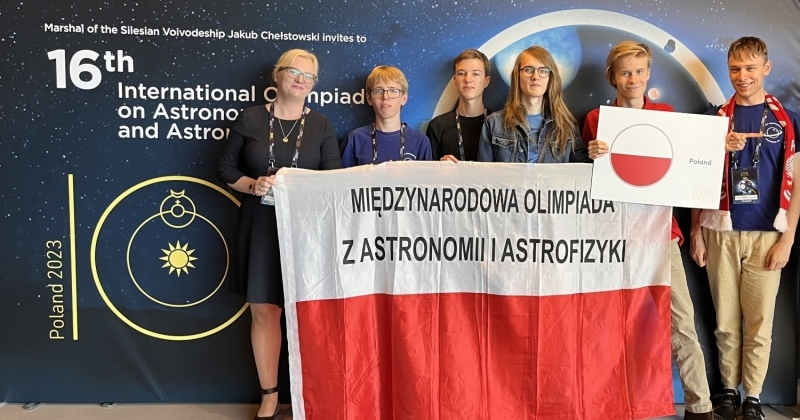 Stojący laureaci Olimpiady wraz z opiekunem dr Karolina Bąkowską. Wszyscy trzymają polską flagę.