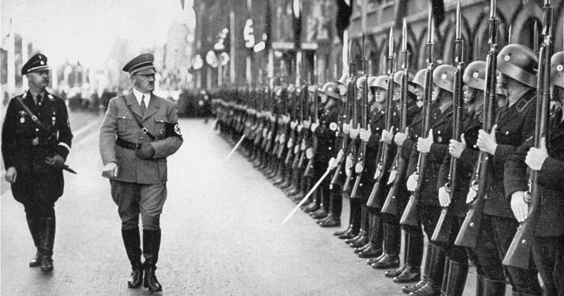 Adolf Hitler z Heinrichem Himmlerem idą obok żołnierzy SS stojących po prawej stronie i trzymających karabiny z nałożonymi bagnetami skierowanymi w górę