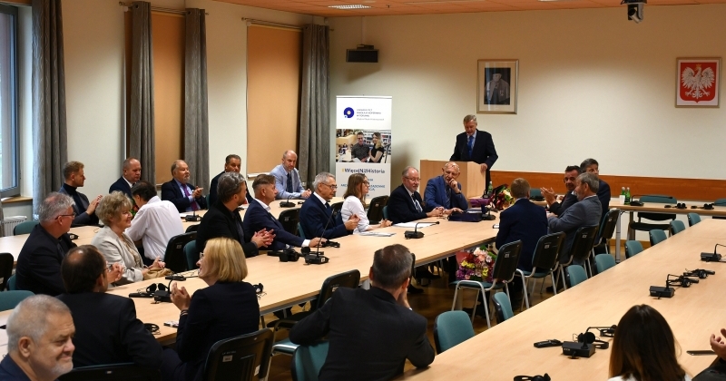 Kilkanaście osób, mężczyzn i kobiet w różnym wieku, słucha na siedząco przemówienia prowadzącego spotkanie profesora Andrzeja Radzimińskiego, który stoi przy mównicy.