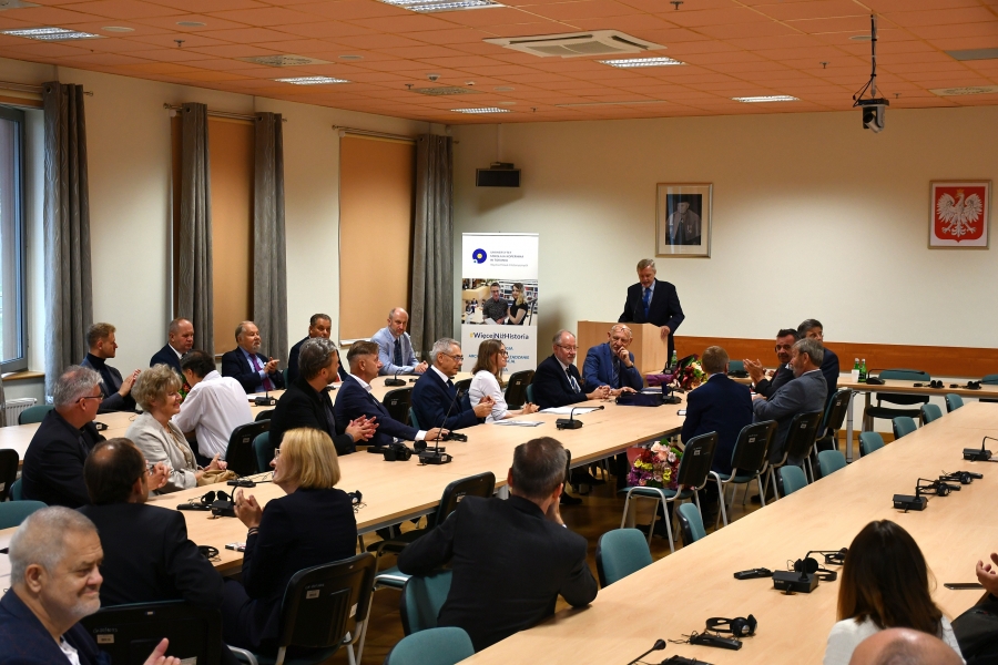 Kilkanaście osób, mężczyzn i kobiet w różnym wieku, słucha na siedząco przemówienia prowadzącego spotkanie profesora Andrzeja Radzimińskiego, który stoi przy mównicy.